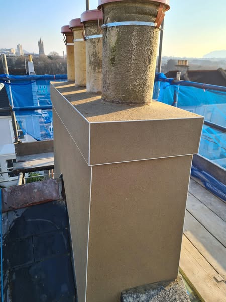 A close-up view of a rooftop chimney stack with multiple round chimney pots, surrounded by scaffolding and blue safety netting, overlooking a cityscape in the background.
