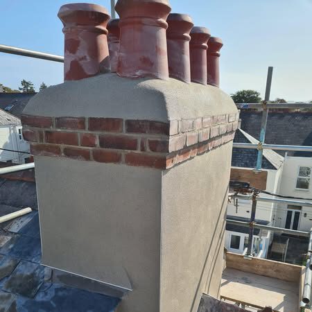 Chimney stack on a rooftop with six red chimney pots, fresh render and clean brickwork, surrounded by scaffolding against a clear blue sky.